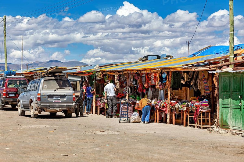 Various market stalls with visitors and cars, lively rural atmosphere under a cloudy sky, market stall for tourists in the Salar de Uyuni in Bolivia