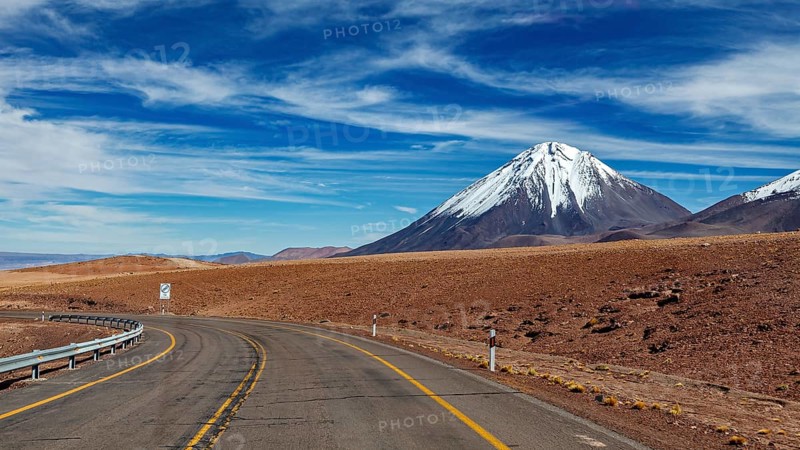 Deserted road leads to a snow-covered mountain under a clear sky, The landscape with the volcanoes on the Altiplano in Bolivia