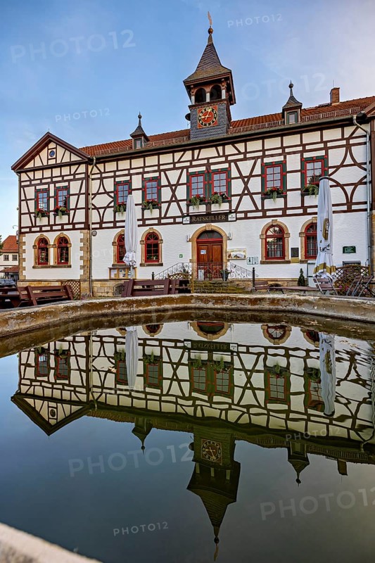 Historic half-timbered building reflected in the calm water basin against a blue sky, Historic half-timbered house in the village of Mühlburg in Thuringia near Erfurt