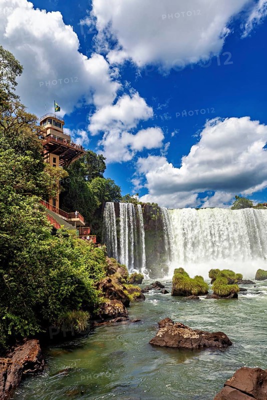 Impressive waterfall with neighbouring building and flag, blue sky and lush greenery, The Iguazu Falls between Argentina and Brazil