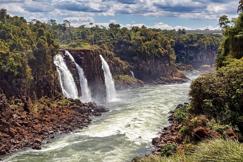 Two waterfalls plunge into a river, surrounded by a green and rocky landscape, The Iguazu Falls between Argentina and Brazil