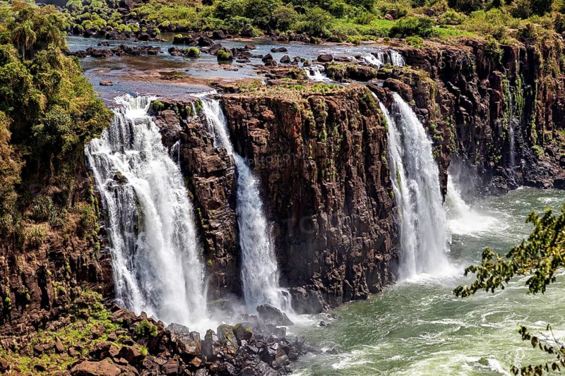 Wide waterfalls cascade over steep cliffs into a bubbling river, The Iguazu Falls between Argentina and Brazil