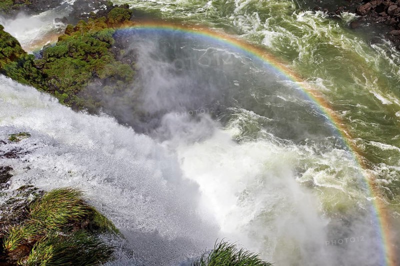 A glowing rainbow appears over a thundering waterfall, The Iguazu Falls between Argentina and Brazil