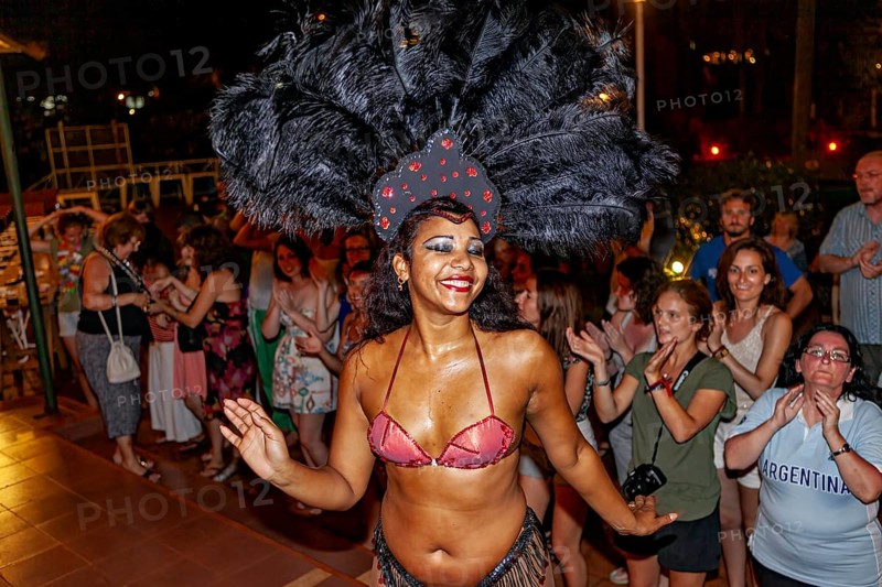 Dancer with feather headdress dances in front of an applauding audience, Samba dancers to entertain tourists at the waterfalls of Iguazu in Argentina