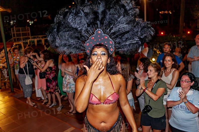Woman in exotic costume with feather headdress gives kisses to the crowd, samba dancers to entertain tourists at the waterfalls of Iguazu in Argentina