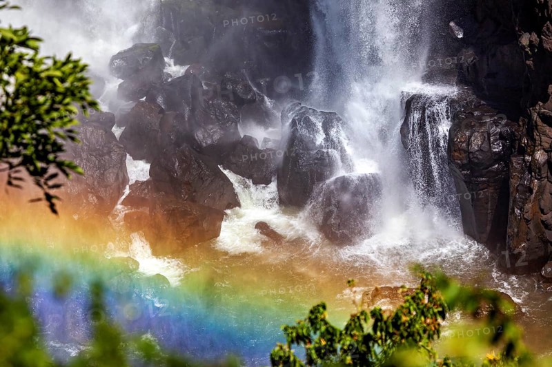 Waterfall meets dark rocks, a rainbow shines in the foreground, The Iguazu Falls between Argentina and Brazil