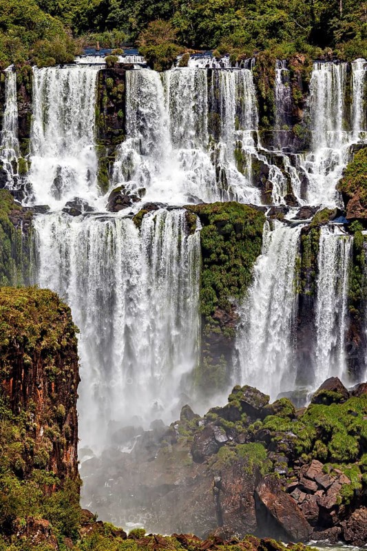 Cascades tumble over steep cliffs, surrounded by dense green vegetation and rising mist, The Iguazu Falls between Argentina and Brazil