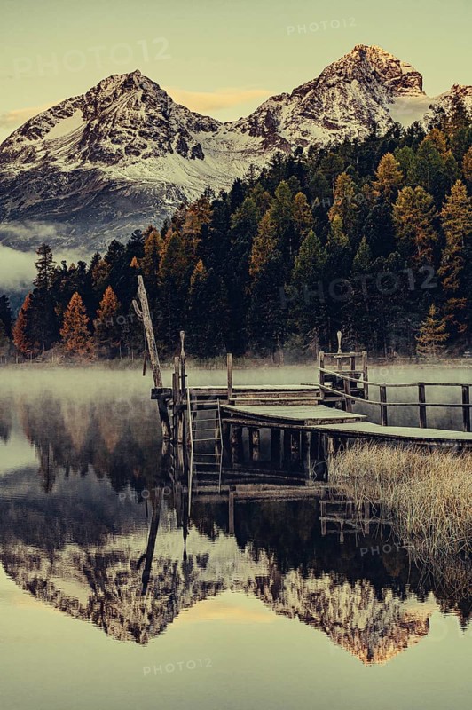 Lake Staz near Sankt Moritz in the Engadin in Switzerland. Morning atmosphere with fog in autumn. Water reflection and snow-covered mountains in the background
