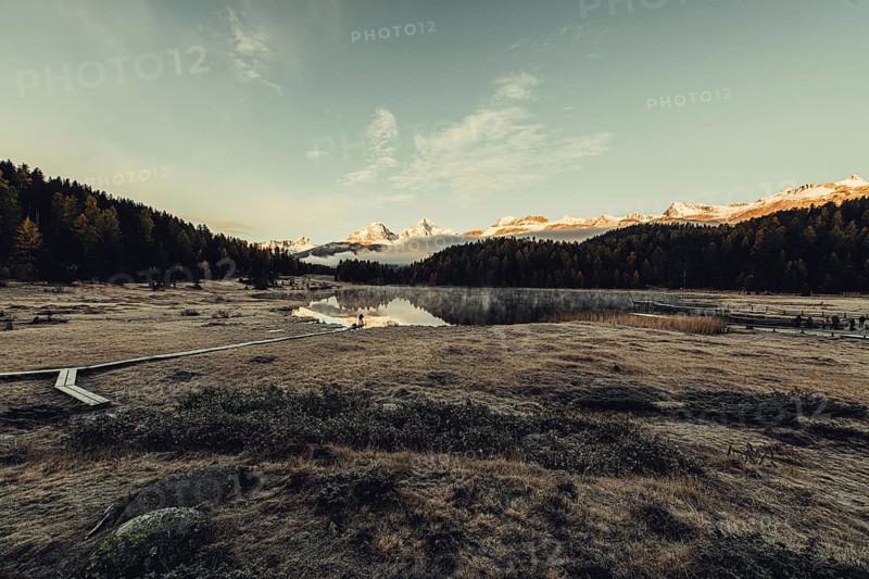 Lake Staz near Sankt Moritz in the Engadin in Switzerland. Morning atmosphere with fog in autumn. Water reflection and snow-covered mountains in the background