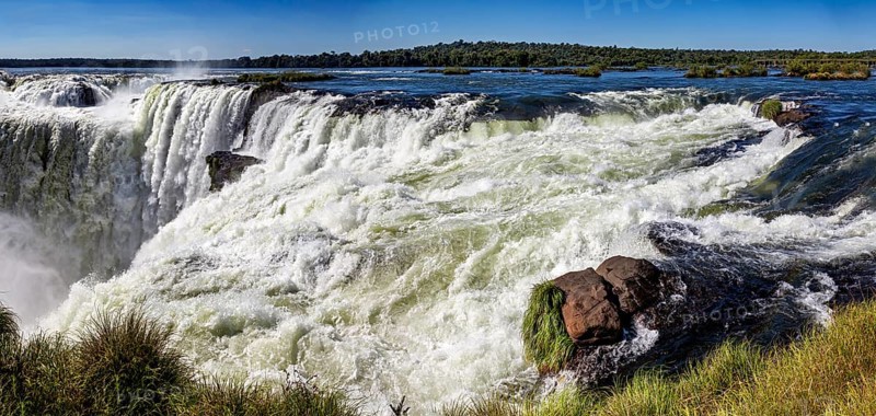 Panoramic view of the raging river and waterfall, surrounded by rocks and lush greenery, The Iguazu Falls between Argentina and Brazil