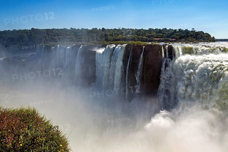 Spectacular view of a waterfall with heavy fog and green banks under a blue sky, The Iguazu Falls between Argentina and Brazil