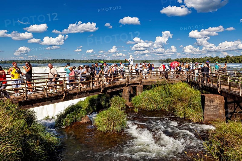 Group of tourists on a wooden bridge over a river with blue sky and clouds, tourist jetty at the Iguazu Falls between Brazil and Argentina