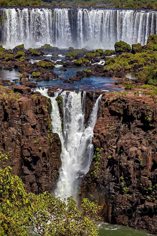 Waterfalls cascade over steep cliffs into a river surrounded by dense trees and plants, The Iguazu Falls between Argentina and Brazil