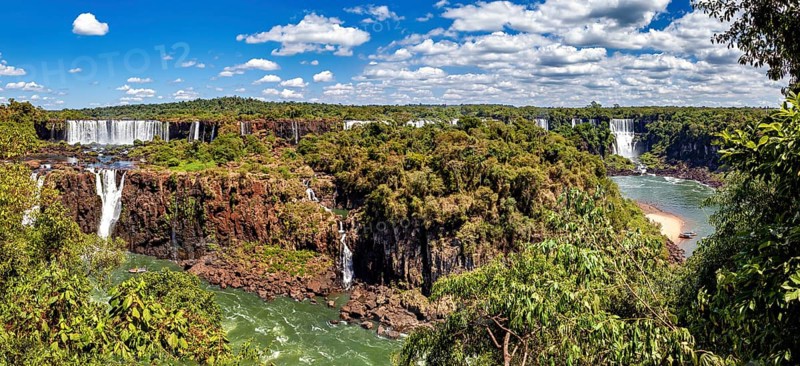 Sweeping views of waterfalls and river, surrounded by lush vegetation under a cloudy sky, The Iguazu Falls between Argentina and Brazil