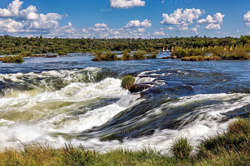Powerful waterfall riverbed with surrounding trees and blue sky, The Iguazu River between Argentina and Brazil