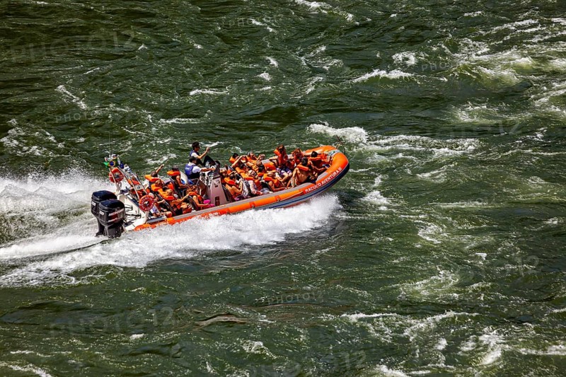 People in an orange-coloured rubber dinghy navigate through turbulent river waters, tourists in a speedboat on the Iguazu River in Argentina