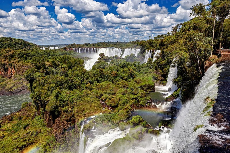 Several magnificent waterfalls and rainbows amidst lush vegetation under clear skies, The Iguazu Falls between Argentina and Brazil