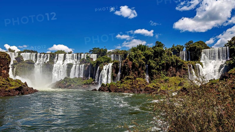 Majestic waterfalls with splashing water surrounded by green vegetation and blue sky, The Iguazu Falls between Argentina and Brazil