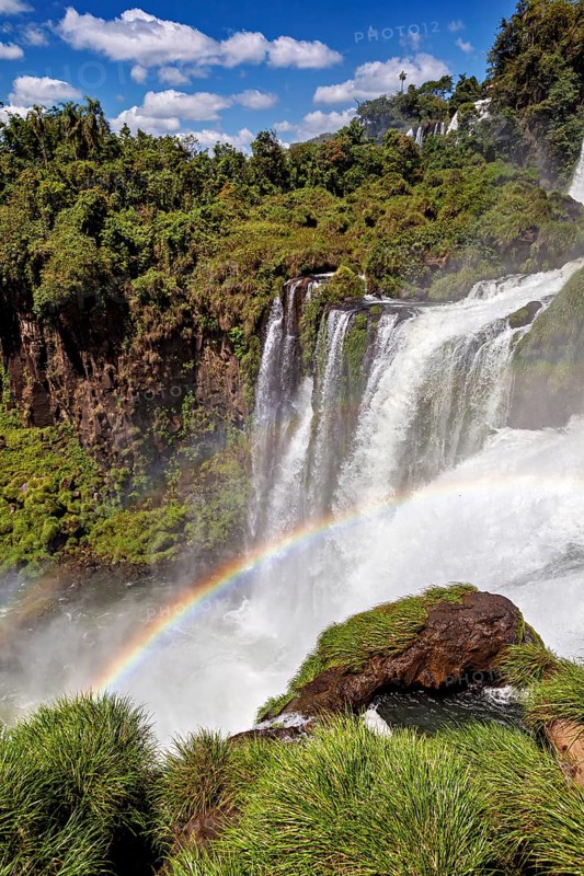 Cascading waterfall over rocks with rainbow and surrounding green forest, The waterfalls of Iguazu between Argentina and Brazil