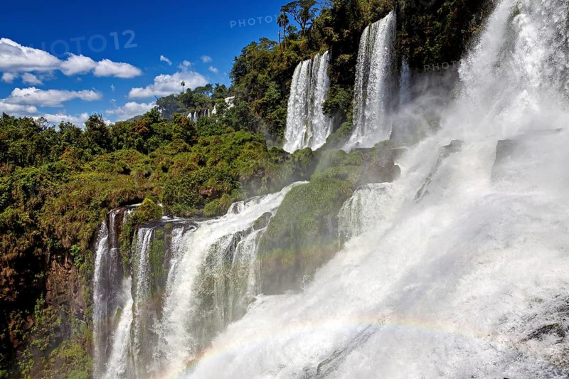 Waterfalls with dense fall and rainbow, embedded in lush forest under a blue sky, The waterfalls of Iguazu between Argentina and Brazil