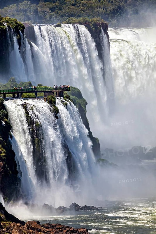 Spectacular waterfall with observation bridge, surrounded by dense vegetation and foaming spray, The Iguazu Falls between Argentina and Brazil