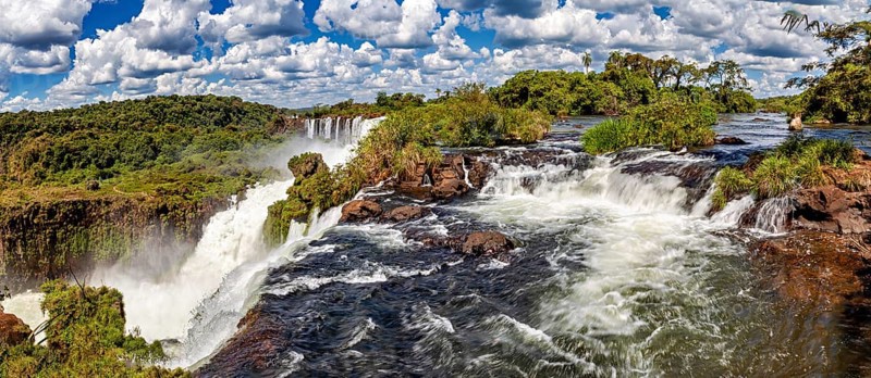Panoramic view of rushing river and waterfall under a dramatic sky, The Iguazu Falls between Argentina and Brazil