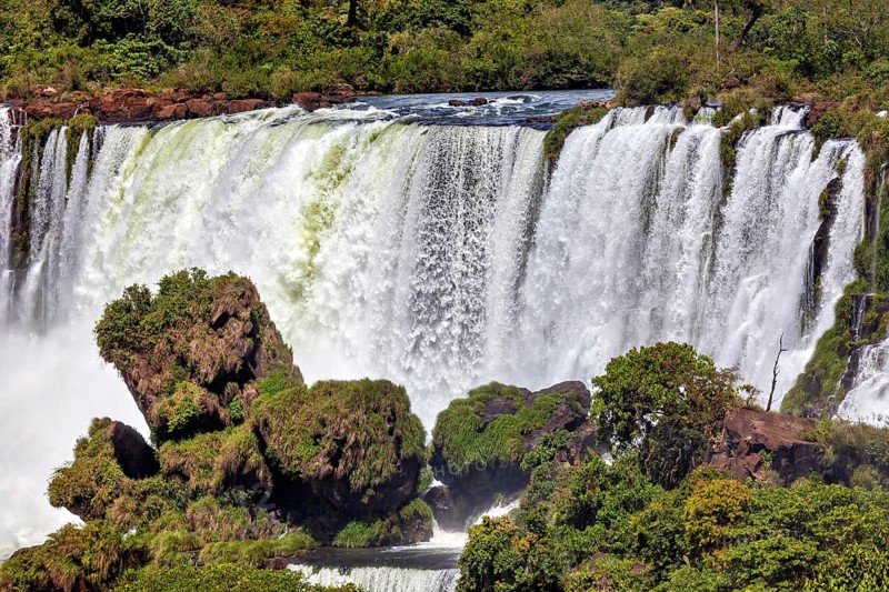 Large waterfall with lush vegetation and rocky ledges, The Iguazu Falls between Argentina and Brazil