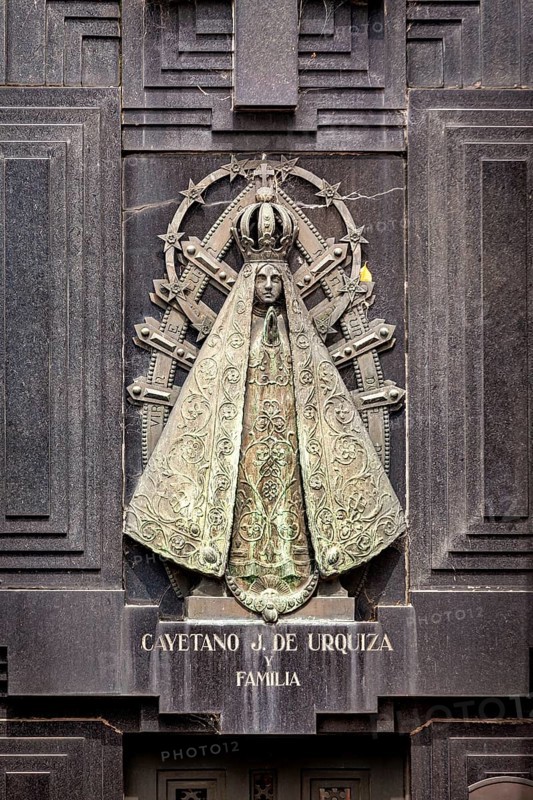 Metal relief of a Madonna on a dark stone surface with engravings and religious symbols, La Recoleta cemetery in Buenos Aires Argentina