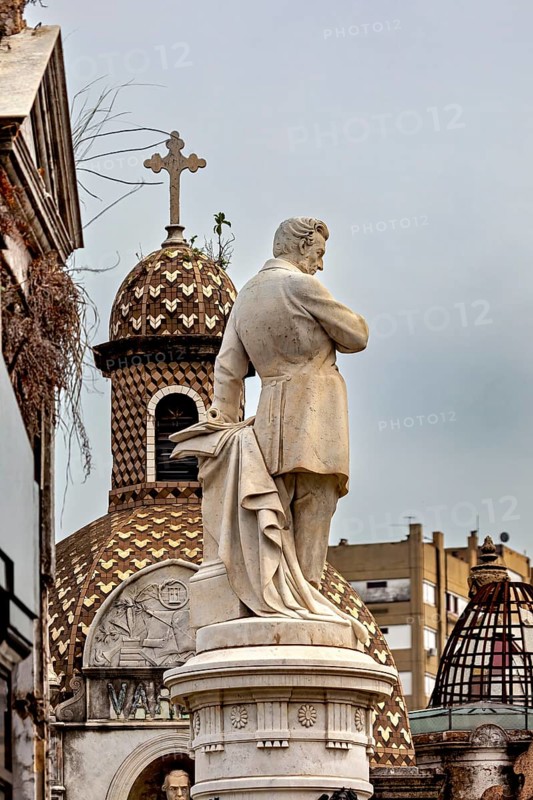Marble sculpture in front of a decorative dome with a cross in an urban setting, La Recoleta cemetery in Buenos Aires Argentina