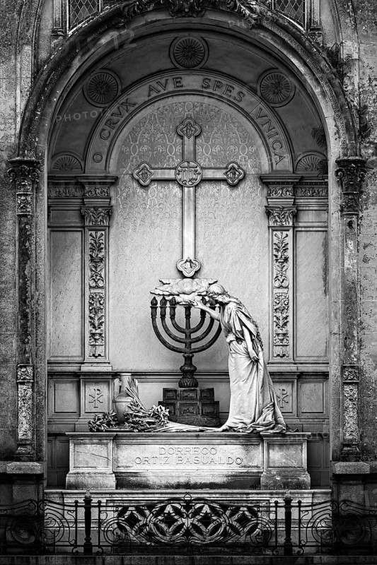 Black and white image of a statue and cross in an ornate mausoleum, La Recoleta Cemetery in Buenos Aires Argentina