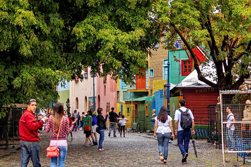 People walking on a colourful street with colourful houses and trees in an urban environment, The colourful city and tango district La Bocca in Buenos Aires Argentina