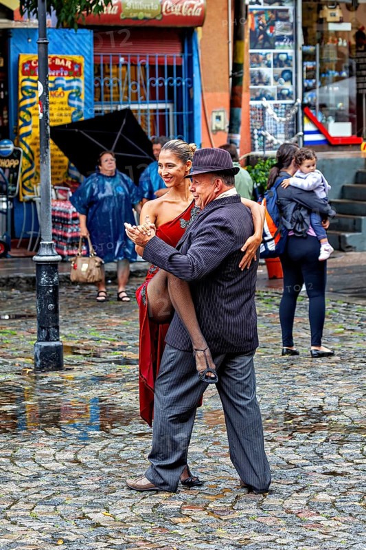 Tango couple in an intimate embrace dancing on a rainy street, surrounded by spectators, The colourful city and tango district La Bocca in Buenos Aires Argentina