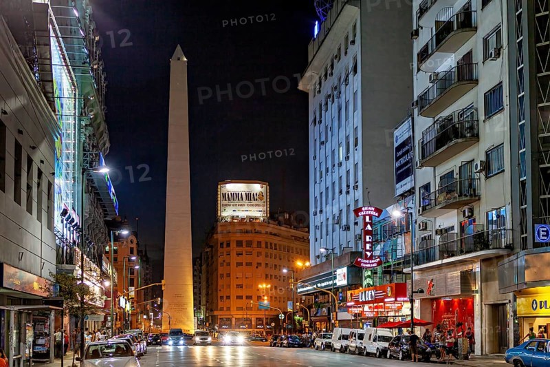 Night scene in a busy shopping street with the obelisk illuminated in the distance, The Great Obelisk in the city of Buenos Aires Argentina