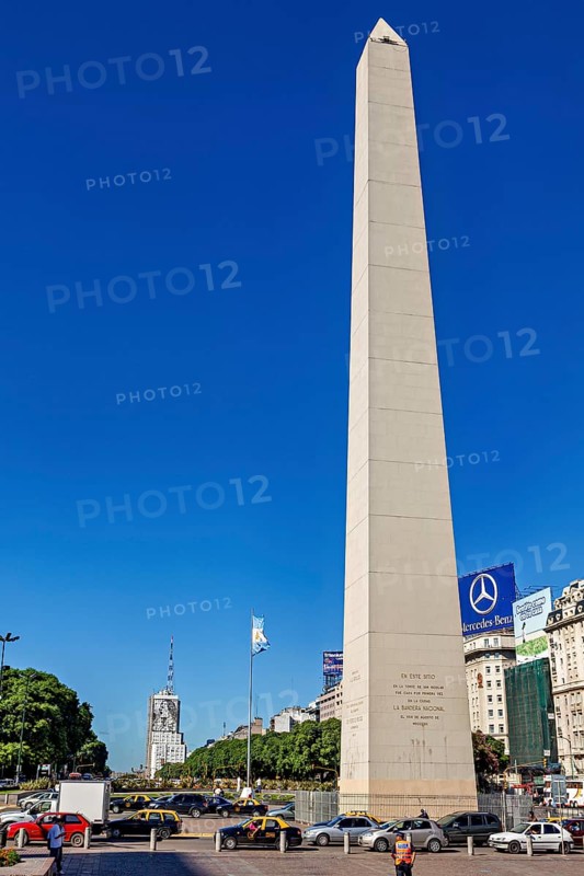 A tall obelisk under a clear sky in Buenos Aires in daylight, flanked by cars, The great obelisk in the city of Buenos Aires Argentina