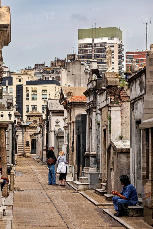 Urban cemetery alley with people and historic graves surrounded by modern architecture, La Recoleta Cemetery in Buenos Aires Argentina