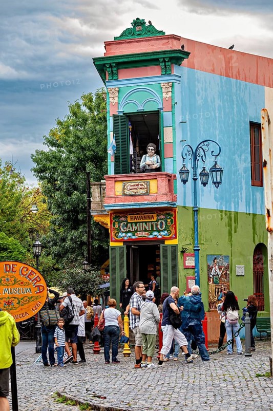 A lively place with colourful buildings and people, a statue stands on the balcony, The colourful city and tango district La Bocca in Buenos Aires Argentina