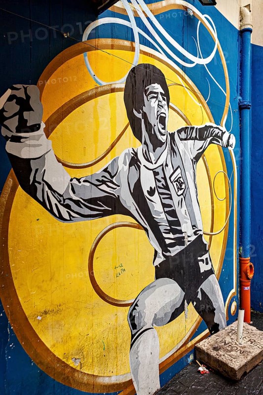Mural of a cheering football player on a yellow and blue background, The football stadium of La Bocca of the Bocca Juniors in Buenos Aires Argentina