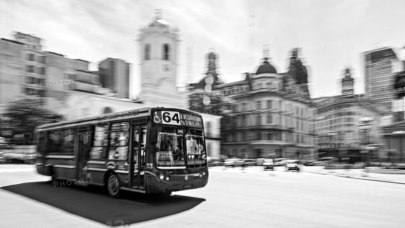 A bus drives through a busy city with historic buildings in the background in black and white, Bus route 64 in the city centre of Buenos Aires in Argentina
