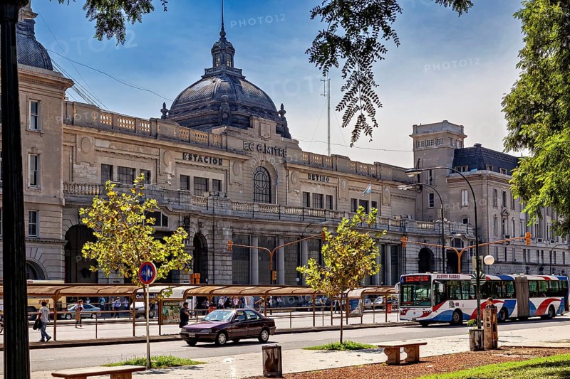 A historic railway station with a domed roof, surrounded by cars and trees in daylight, The city of Buenos Aires in Argentina