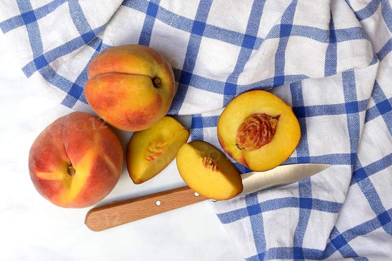 Peach with knife on kitchen towel, peach halves, Prunus persica