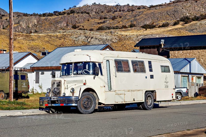 A vintage camper van parked in a mountainous landscape, surrounded by houses and clear skies, A historic Mercedes bus in El Chalten in Patagonia Argentina
