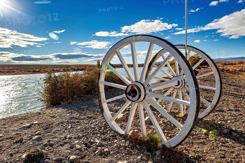 White wagon wheels on the riverbank under a blue sky with clouds, Historic horse-drawn wagon or carriage with wagon wheels in Patagonia