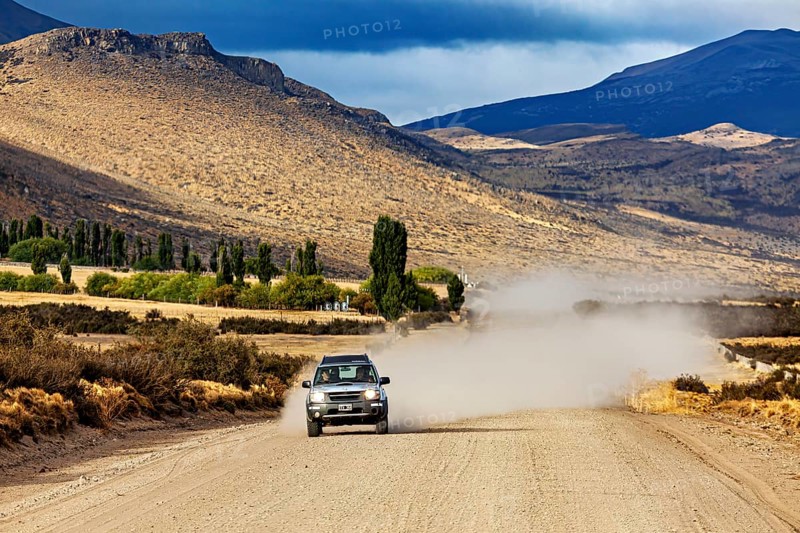 A car drives on a dusty gravel road through a mountainous landscape, Over gravel tracks through Patagonia in Argentina
