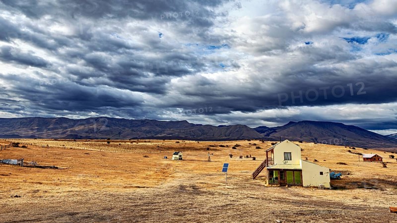 A small house in an open, rural landscape under a dramatically cloudy sky, The Patagonian landscape near El Chalten in Argentina