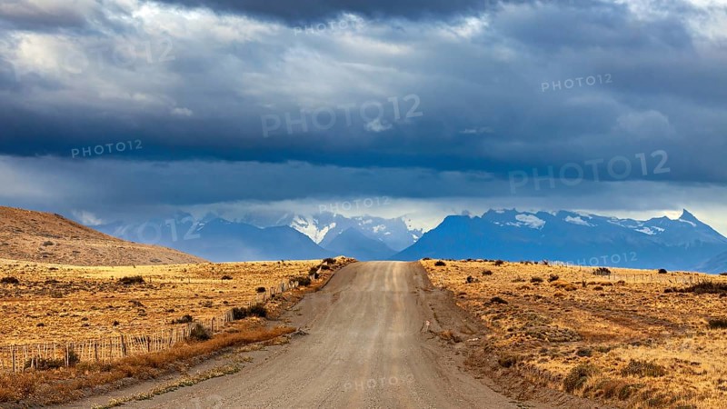 A long gravel road leads to a distant mountain range under a cloudy sky, The Patagonian landscape near El Chalten in Argentina