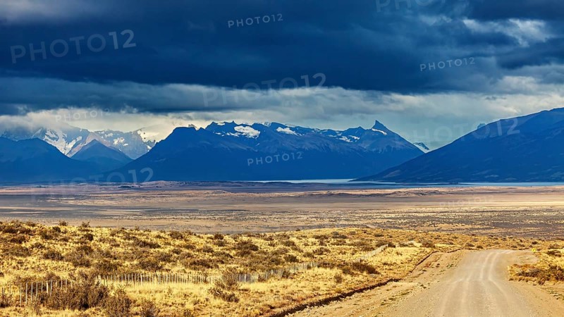 A gravel road leads to a mountain range under a dramatic cloudy sky, The Patagonian landscape near El Chalten in Argentina
