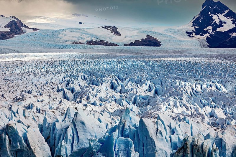 A vast icy landscape stretches out in front of a cloudy sky and majestic mountain peaks, The Perito Moreno glacier in Argentina