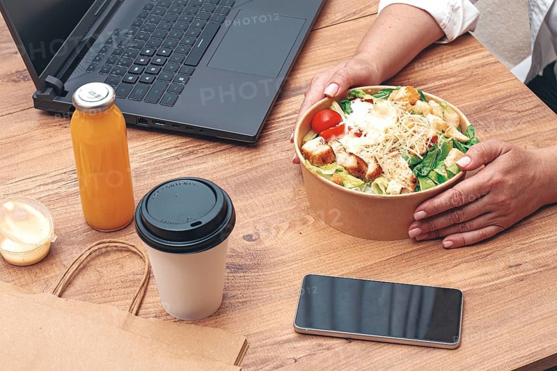 A woman is working on a laptop at home, there is food on the table, salad, coffee and juice, delivery, work at home