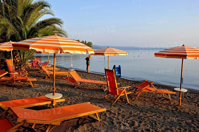 Beach, deckchairs, sunshades at the lido, Lake Bolsena, Lago di Bolsena, volcanic crater lake, calm smooth water surface, warm evening light, Bolsena, Province of Viterbo, Lazio, Italy