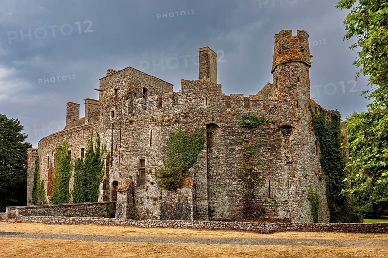 Stone castle with round towers and ivy growth under a cloudy sky, Pirou Castle in Normandy, France